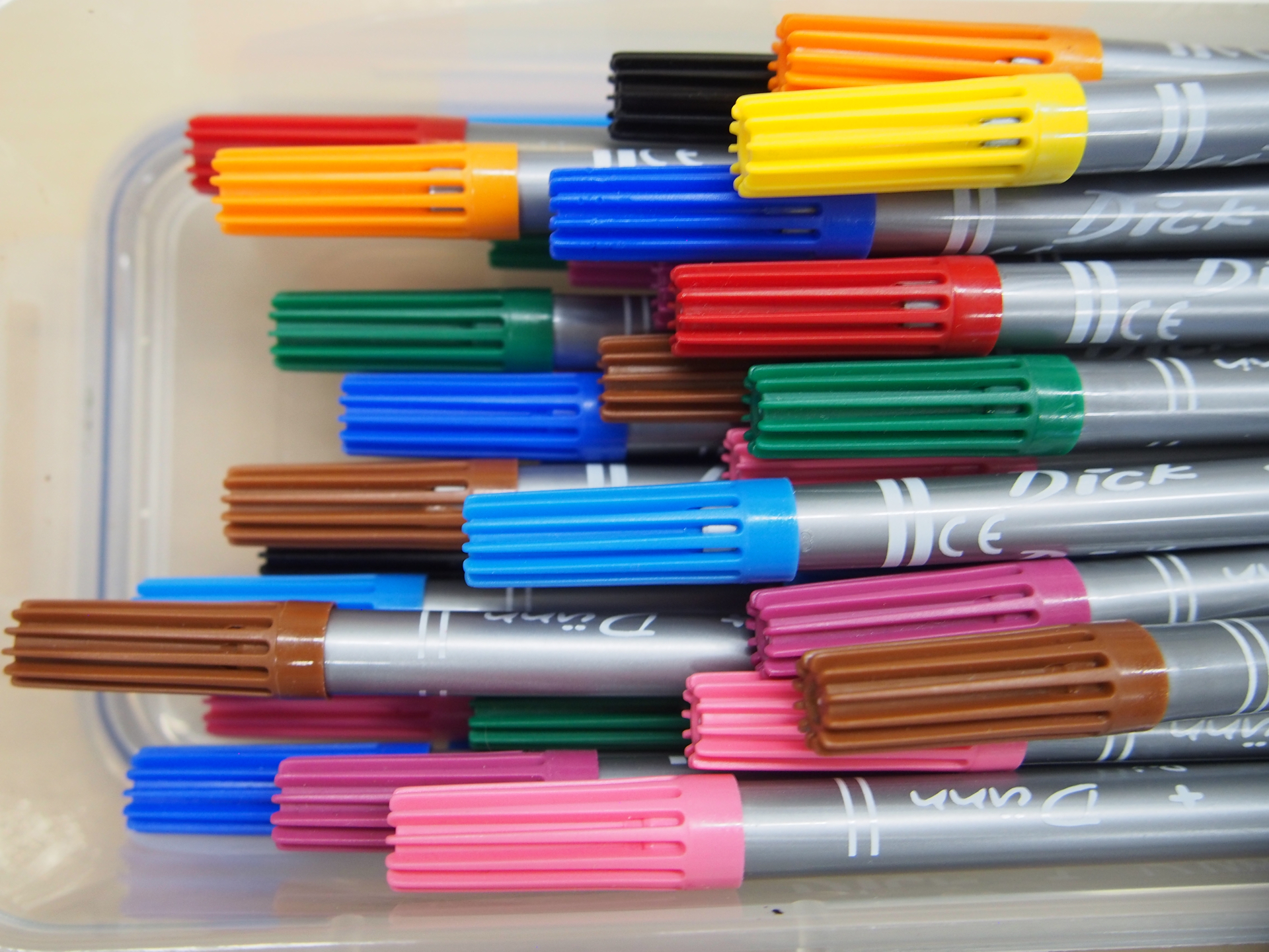 Viele bunte Filzstifte liegen dicht nebeneinander in einer durchsichtigen Schale